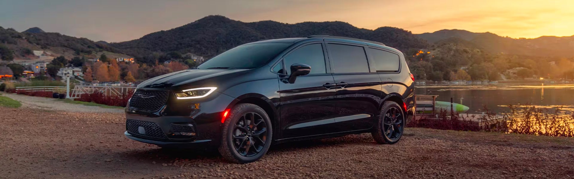 Black Chrysler Pacifica minivan with black wheels parked near a lake at sunset