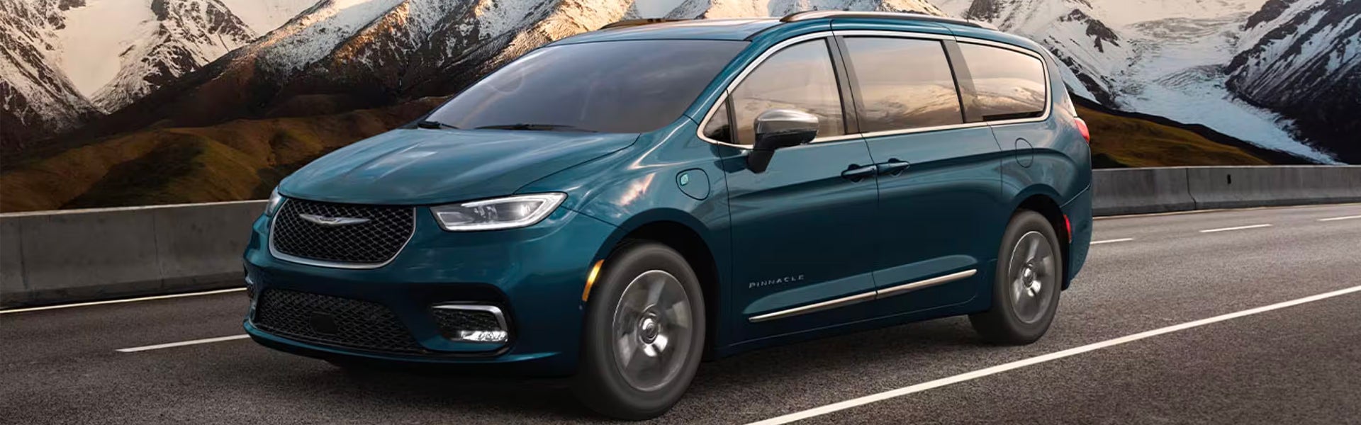 Dark teal minivan driving on highway with mountains in background