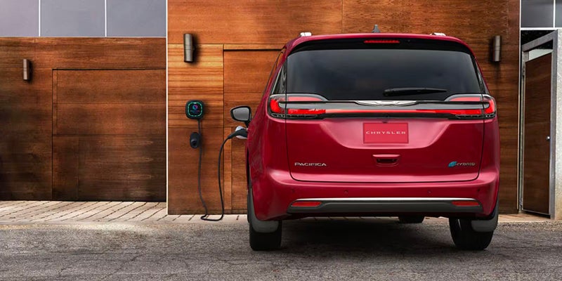 Rear view of red Chrysler minivan charging at home station