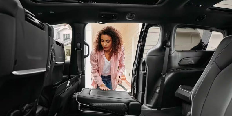 This image shows the interior of a vehicle, likely a minivan or large SUV, highlighting its passenger and cargo versatility. Here's what is visible: Interior View: The photo is taken from inside the vehicle, looking towards the open side door and out to a suburban setting