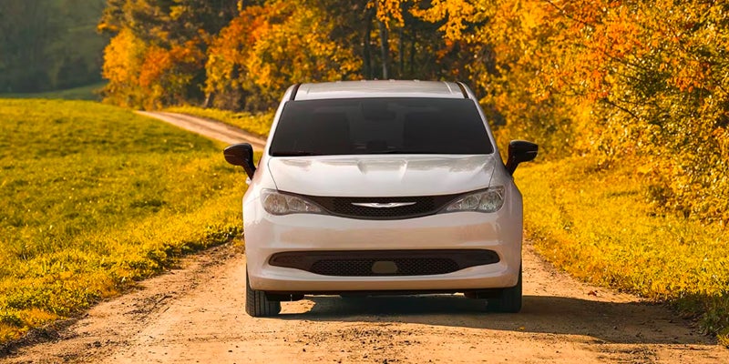 White Chrysler Pacifica minivan on a dirt road in autumn