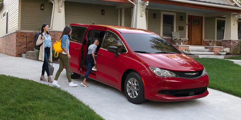 Red minivan with family outside suburban home