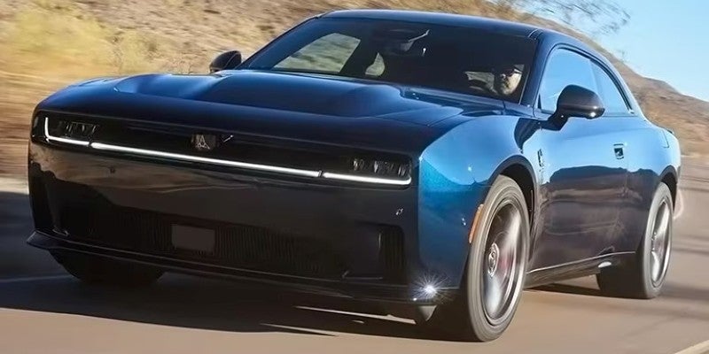 A dark blue coupe driving fast on a desert road in the sun