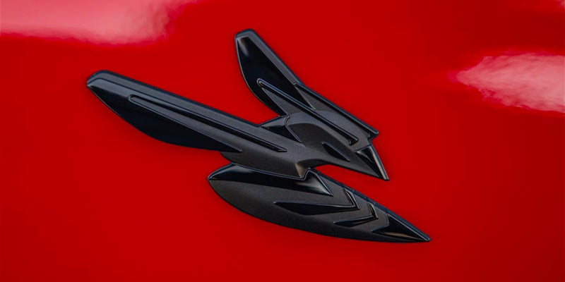 A close-up of a black Dodge Hornet emblem on red paint