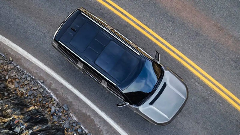 Aerial view of a gray car with a dark roof driving on a curving road next to a rocky slope.
