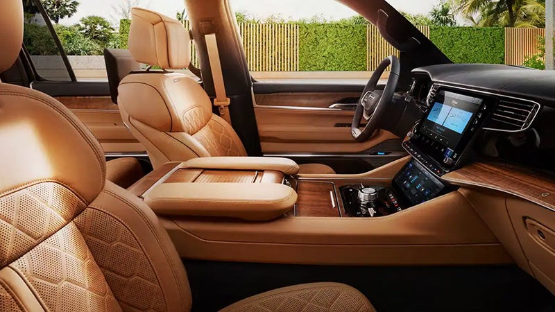 Interior of a luxury car with tan leather seats, wooden trim, and multiple digital screens.
