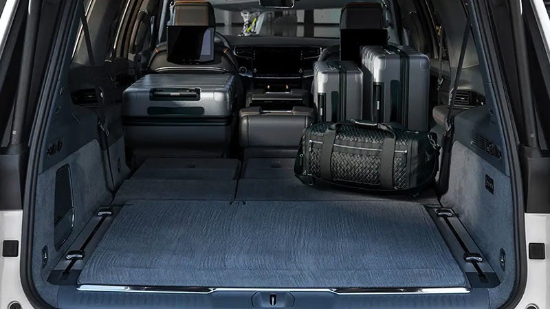 The cargo area of a large SUV with the rear seats folded flat and various luggage bags stored within.