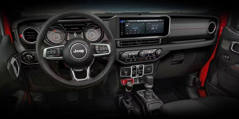 The interior of a Jeep, featuring a black steering wheel with "Jeep" in the center and a large infotainment screen.