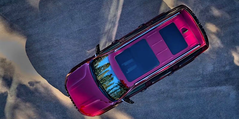 Top-down view of a shiny burgundy SUV parked on an asphalt or concrete surface with a tree reflection.