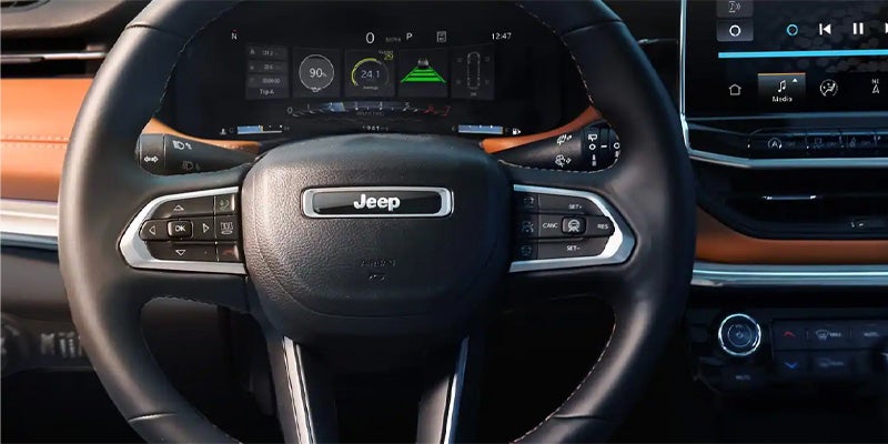 Steering wheel of a Jeep with a digital dashboard showing system details, and a touchscreen infotainment system.