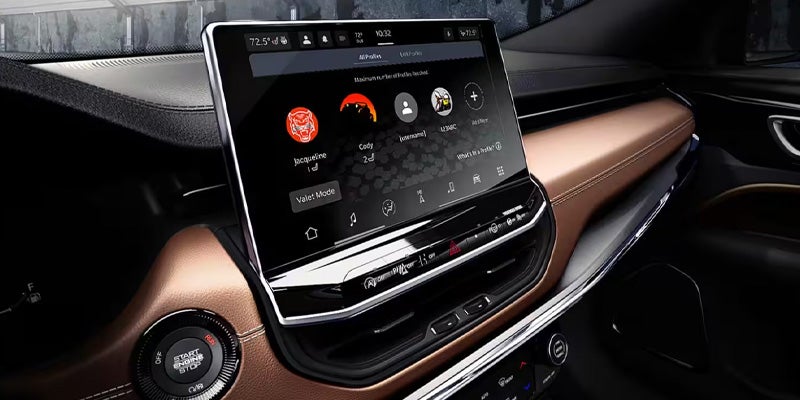 View of a car's interior, showing a large central touchscreen displaying user profiles and a "Start Engine/Stop" button.