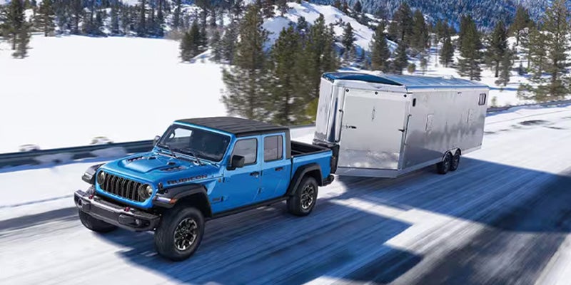 Blue Jeep Gladiator truck towing a trailer on a snowy road