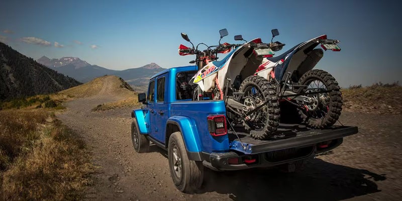 Blue Jeep Gladiator truck carrying two dirt bikes in its bed