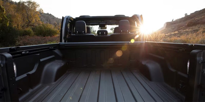 View of a Jeep truck bed with a tonneau cover in the sunset