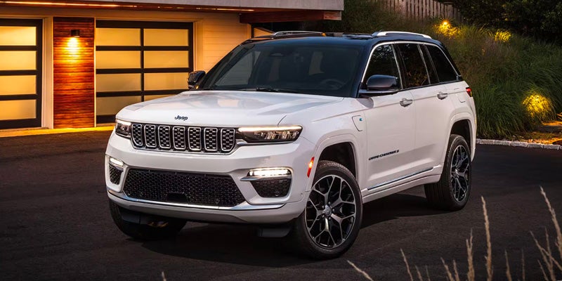 A white 2022 Jeep Grand Cherokee 4xe, a plug-in hybrid SUV, is parked in a driveway at dusk.