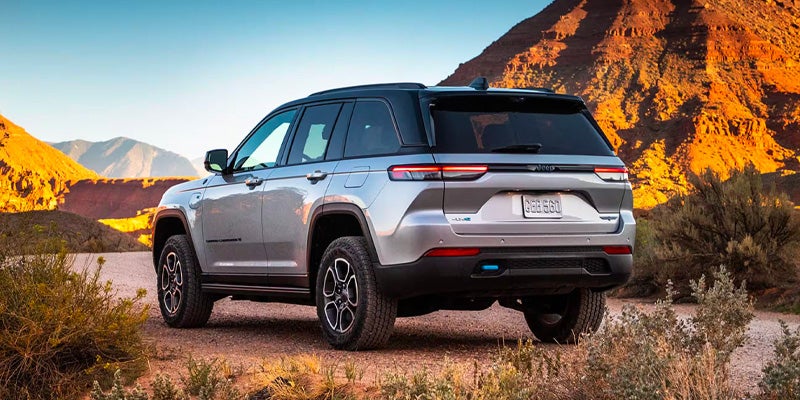 Rear view of a silver SUV parked on a dirt road, with mountains in the background.