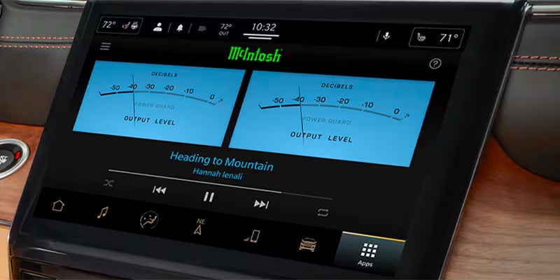 Vehicle infotainment center displaying audio playback with two decibel gauges, "McIntosh" logo, and "Heading to Mountain" song.