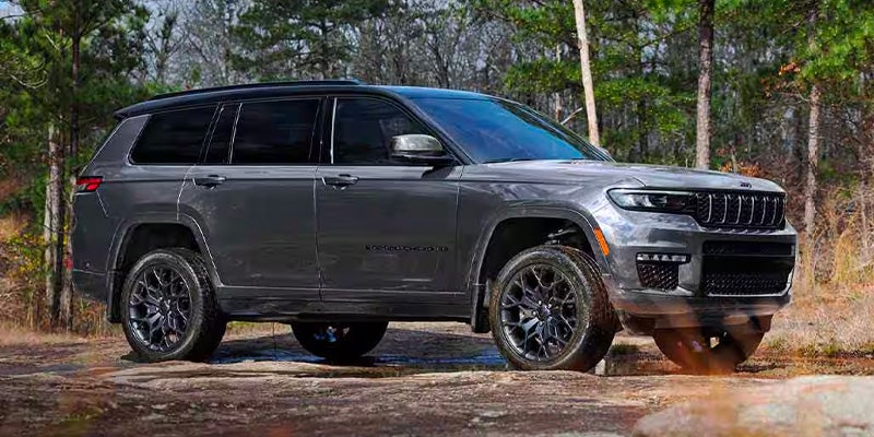 A dark grey 2025 Jeep Grand Cherokee Laredo 4x4 parked on a dirt road in a forest.