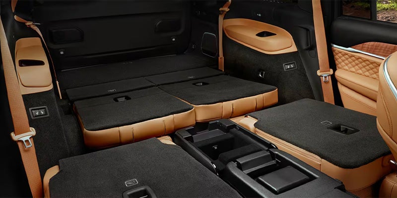 Car interior with tan leather seats folded flat, creating a cargo space with black carpet