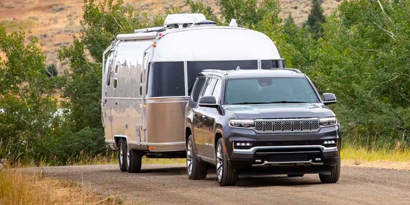 A gray SUV tows a large, shiny silver Airstream trailer on a dirt road.