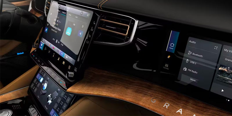 The dashboard of a vehicle displays three digital screens, leather trim, and a wood accent panel.