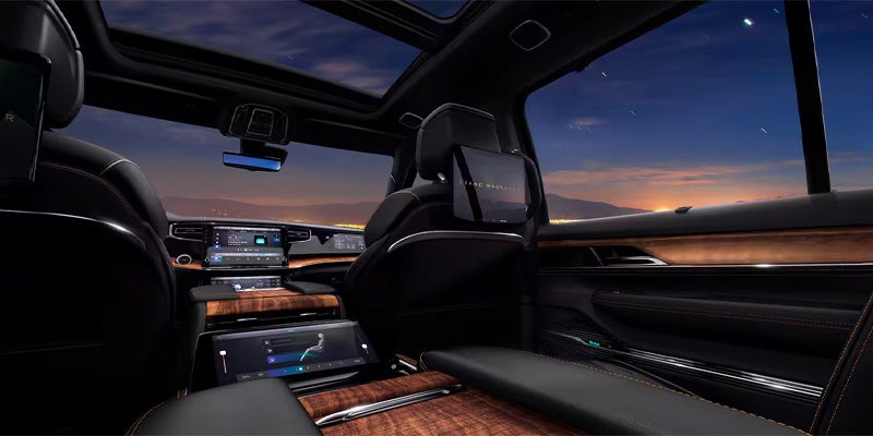 View from the back seat of a luxurious car, featuring wood trim, multiple screens, and a starry night sky outside.