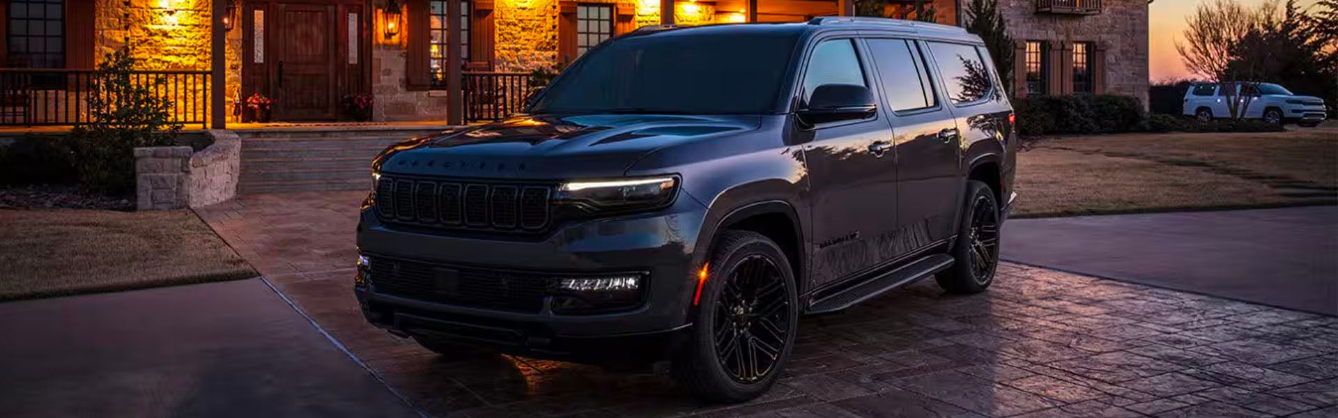 A dark gray SUV parked on a paved driveway in front of a house, lit by warm indoor lights.
