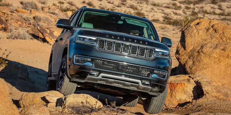 Front view of a black Jeep Wagoneer on a rocky off-road trail, angled slightly downhill.