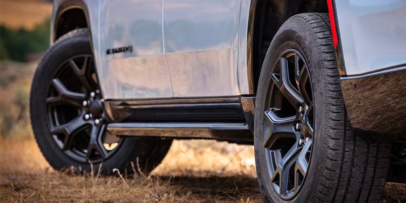 Close-up of a white SUV with large black wheels and running board on a dirt road.