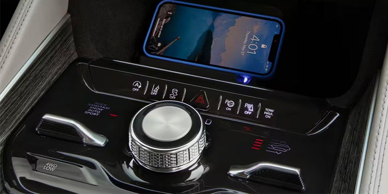 A smartphone charging on a car dashboard with various controls and mode selectors like "Rock," "Sand/Mud," and "Sport."
