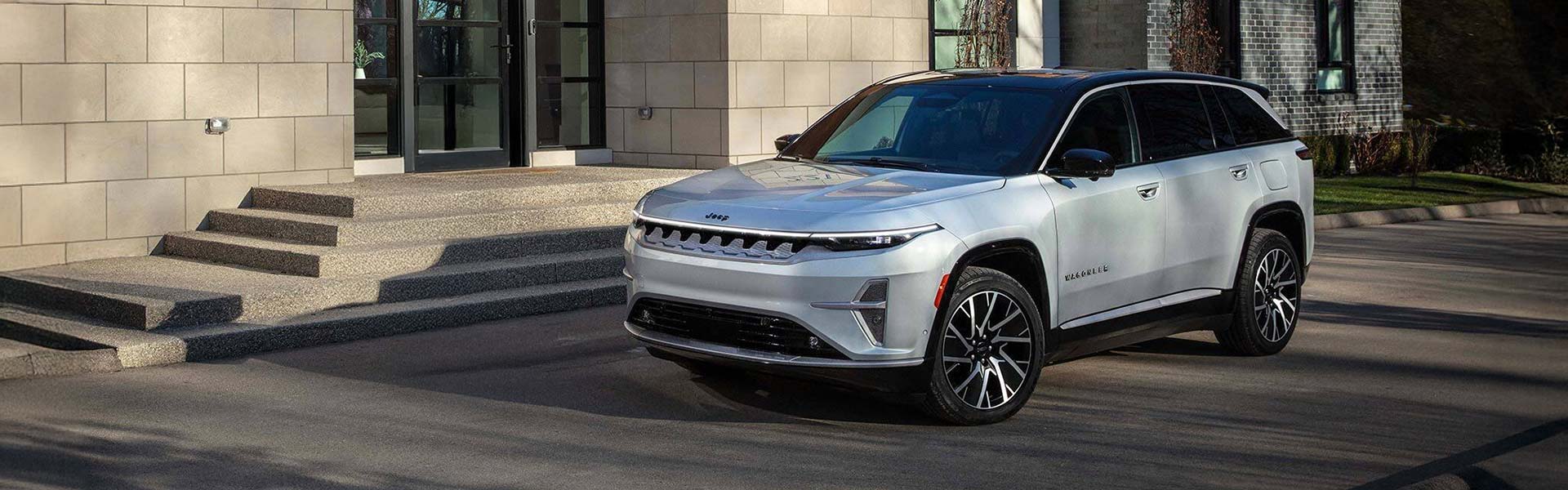 Silver Jeep Grand Cherokee L parked outside a modern building.