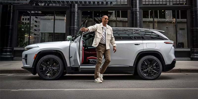 Man stepping out of a silver Jeep Wagoneer S onto a street