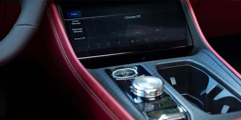 Car interior with a digital screen showing climate controls, and a silver rotary dial on a red and gray console.