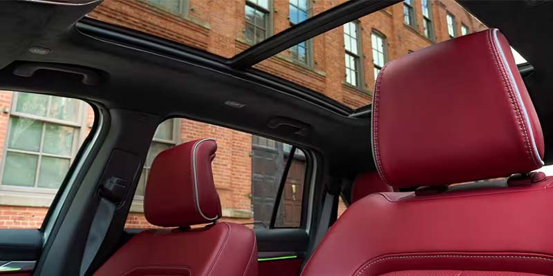Interior of a car with a panoramic sunroof and red leather seats with white piping, viewed from the back seat.