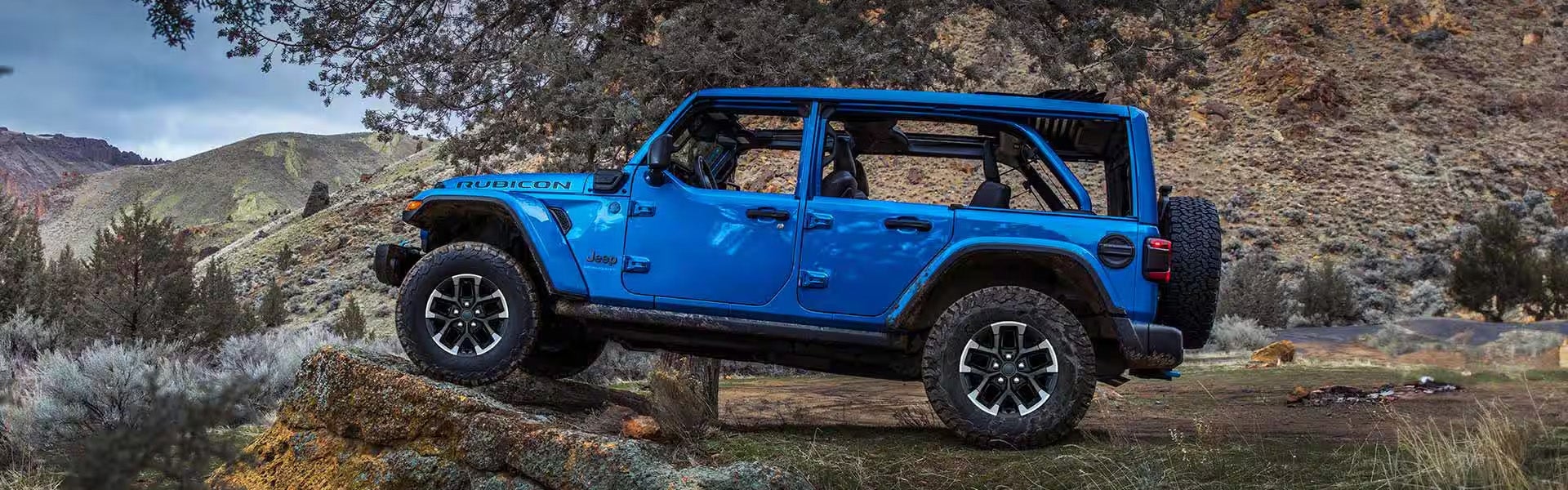 Blue Jeep Wrangler Rubicon with no doors parked on rocks