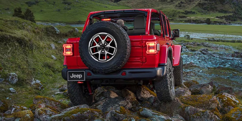 Rear view of a red Jeep Wrangler climbing over rocks