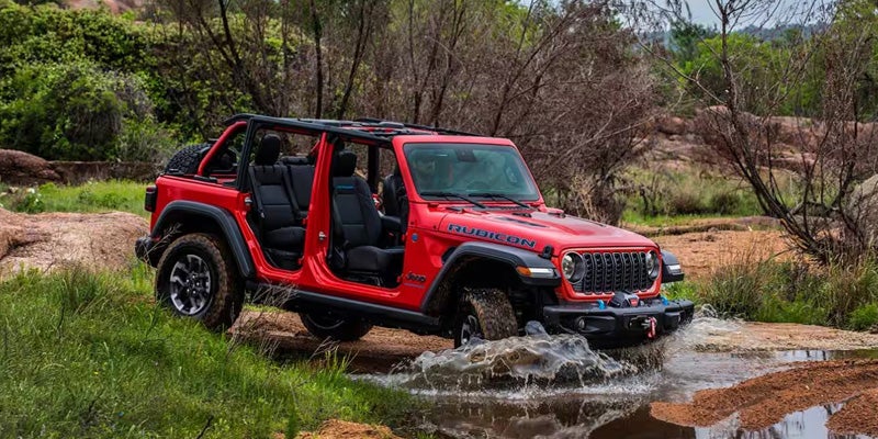 Red Jeep Wrangler with no doors driving through water