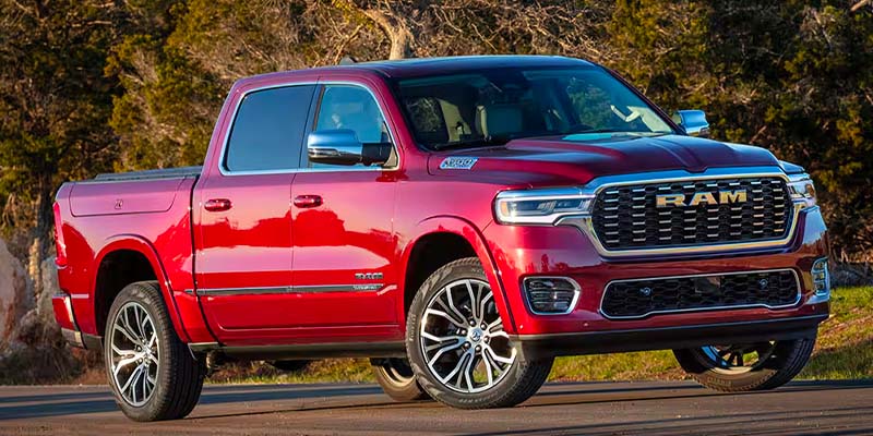 A glossy red Ram 1500 truck with chrome accents and aftermarket wheels is parked on an asphalt road.