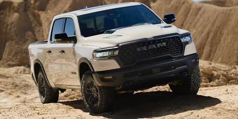 A white Ram pickup truck is angled on a dirt road, with sandy hills in the background.