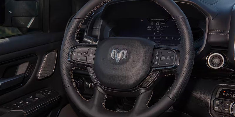 A close-up of a truck's steering wheel and dashboard, showing the leather-wrapped wheel and controls.