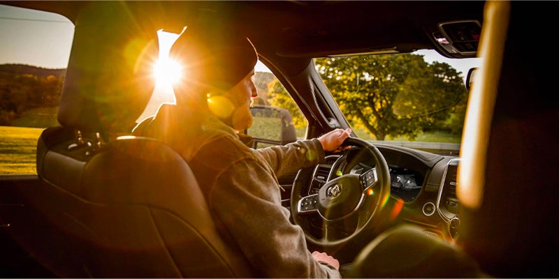 A person in a beanie and jacket drives a car at sunset, sunlight streaming through the window.
