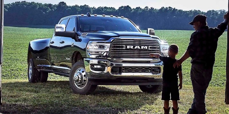 A man and his son stand beside a black RAM truck in a grassy field.