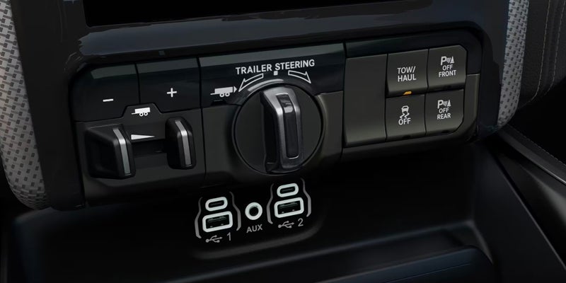 Close-up of a car's control panel, showing buttons for trailer steering, tow/haul, parking assist, and USB ports.