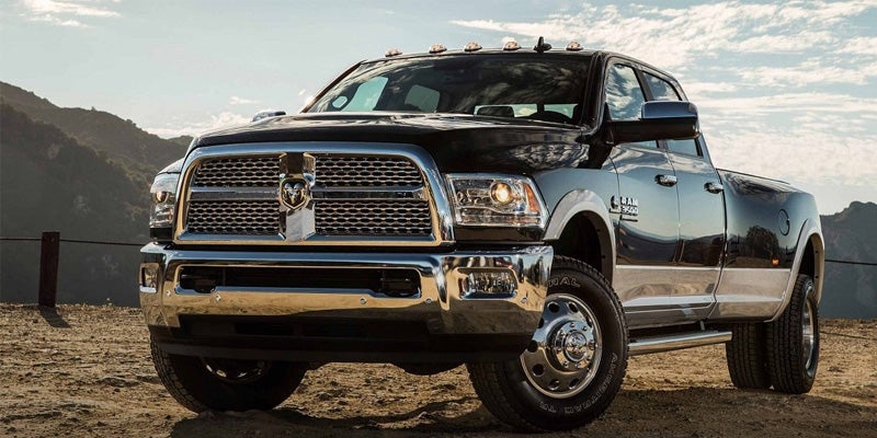 A black quad-cab Ram 3500 pickup truck with shining chrome details, parked off-road in front of mountains.